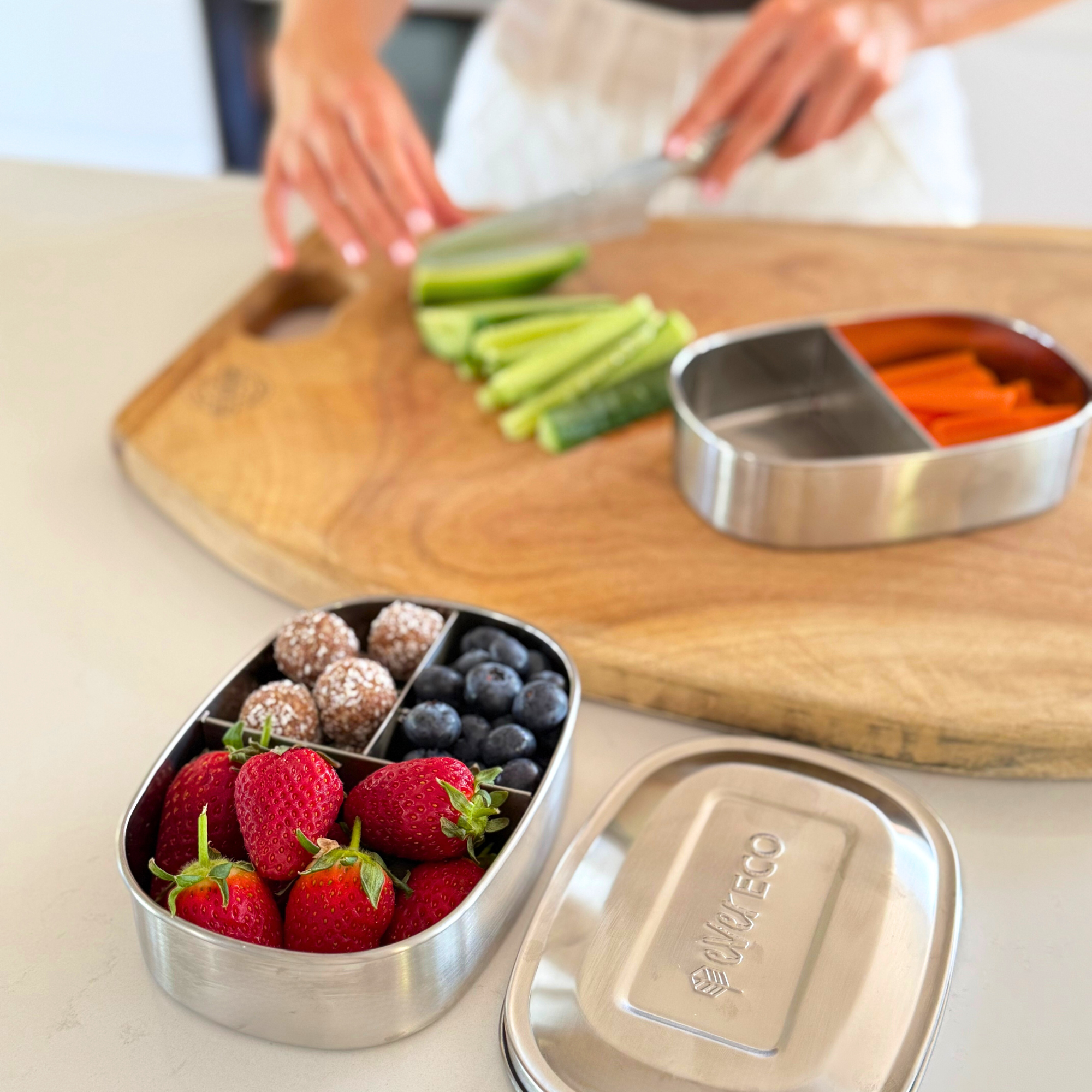 stainless steel bento-style food container with compartments of fruits and berries on a kitchen counter.